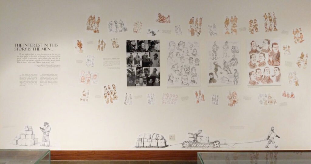 A photo of a wall of a museum with character design studies plastered to it.