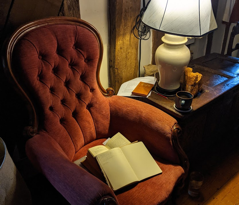 A plush Victorian armchair with a lamp beside it and books on the seat.