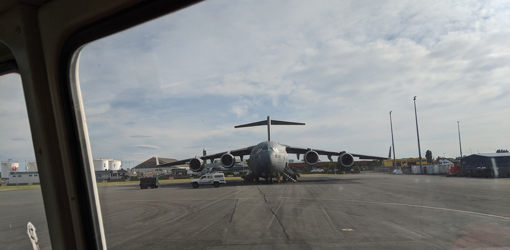 A C-17 on the tarmac, seen head-on through the rear window of a school bus.