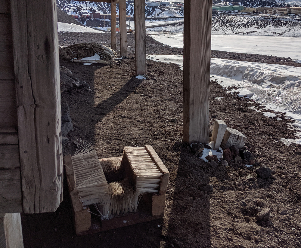 Outside the entrance to the Discovery Hut, looking up under the awning to Winter Quarters Bay, the requisite boot brush sits prominently in the foreground, caught by the diamond-sharp morning light.  One must brush one's footwear thoroughly free of snow and gravel before stepping inside.