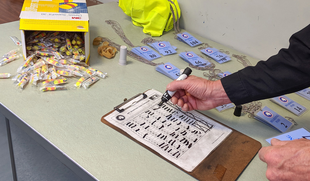 Boarding passes are checked off a list with a whiteboard marker, at the passenger terminal of the USAP headquarters in Christchurch. Behind is a box of earplugs spilling out onto the table.