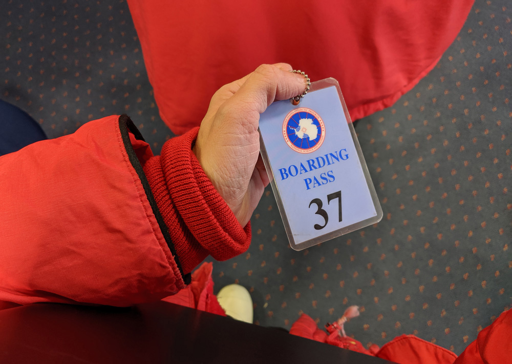 A hand in a red parka sleeve holds a blue USAP boarding pass, number 37