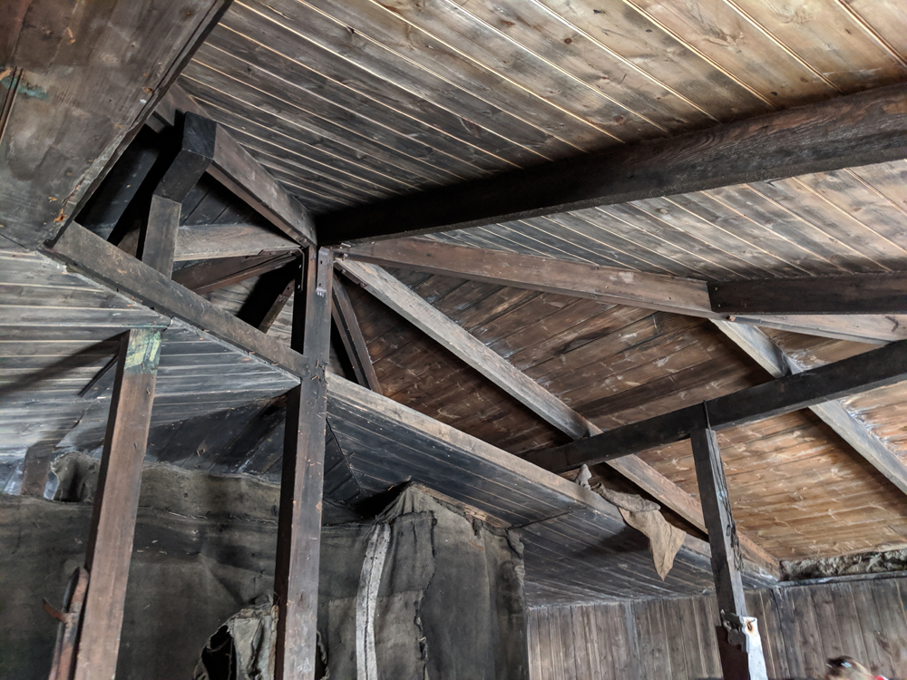The ceiling cavity of the Discovery Hut, which was filled with ice during the Terra Nova Expedition.  There is a central beam going from the peak of the roof to the floor, with four more support beams  making a square around it, and eight roof beams radiating from the central post.  The roof is of a shallow pyramid shape, and the ceiling of a slightly shallower pyramid shape.  A large section of ceiling has been cut away so the construction of the roof is visible.