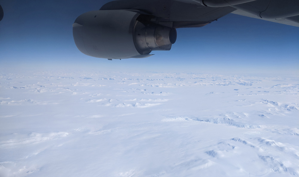 My first sight of the Antarctic continent, somewhere over Victoria Land. A snowy plain interrupted by mountain ranges is spread out below an indigo sky, one of the C-17's engines visible at the top.