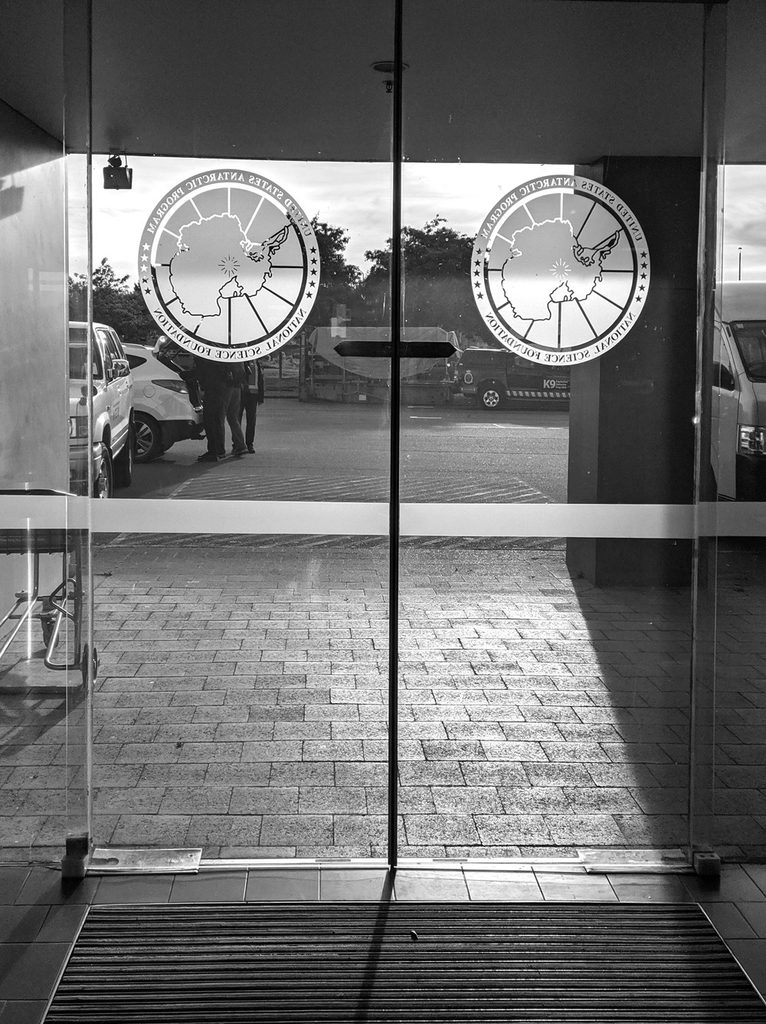 The sun shines through the glass doors of the passenger terminal at the USAP headquarters in Christchurch, highlighting the frosted decals of Antarctica on each.
