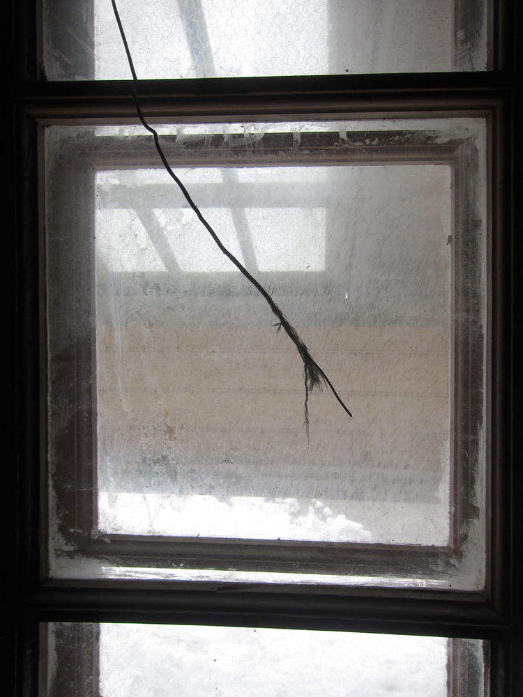 The end of a frayed wire cord hangs backlit in a dusty double-glazed window in the kitchen area of the Discovery Hut.  It may have been the end of the telephone cable that connected to the hut at Cape Evans.
