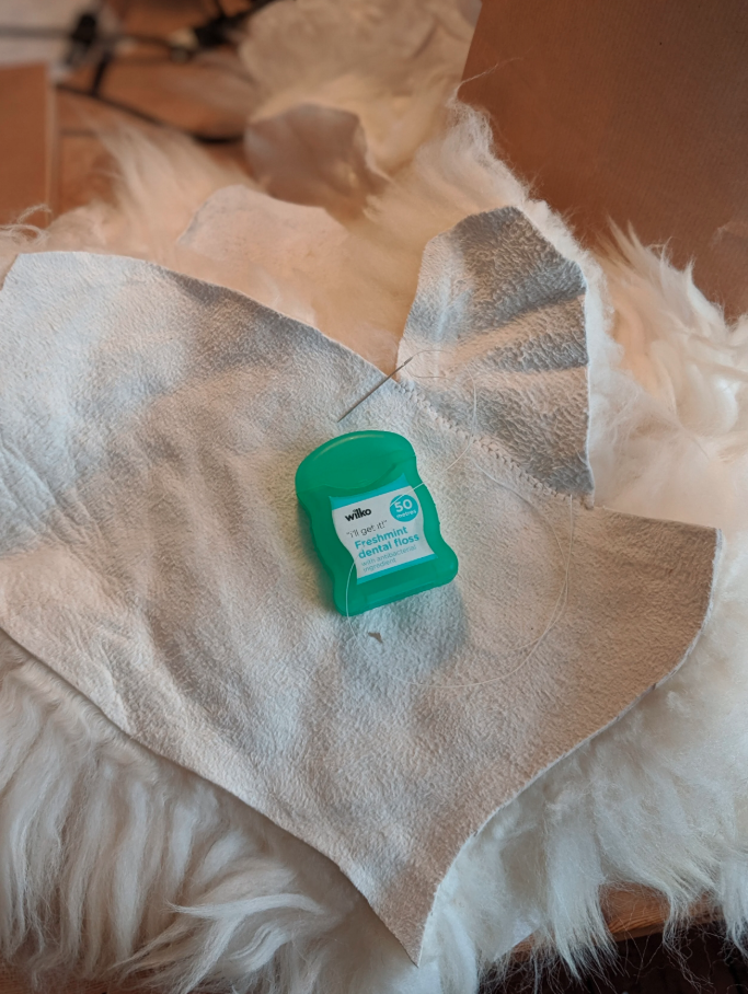 Half a mitt from the leather side, with the thumb piece stitched on.  The dental floss with which it was stitched is sitting on top.