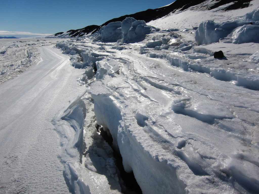 Looking along the length of the tide crack at the foot of Arrival Heights.  Many terraced 'benches' of ice can be seen either side of the crack.  The fast ice on the right is about two feet higher than the sea ice to the left, indicating it is low tide.  Some enormous blocks of ice can be seen piled on the shore at medium distance.
